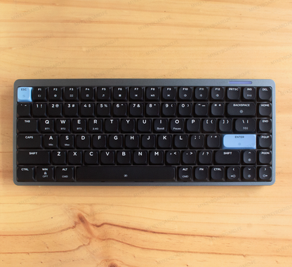 Teclado mecánico Epomaker Luma84 en formato 75% con chasis gris, teclas negras y acentos celestes en fondo de madera.