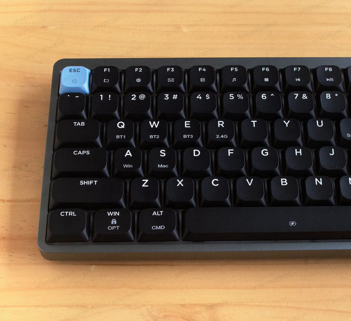 Teclado mecánico Epomaker Luma84 en formato 75% con chasis gris, teclas negras y acentos celestes en fondo de madera.