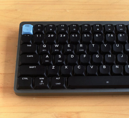 Teclado mecánico Epomaker Luma84 en formato 75% con chasis gris, teclas negras y acentos celestes en fondo de madera.