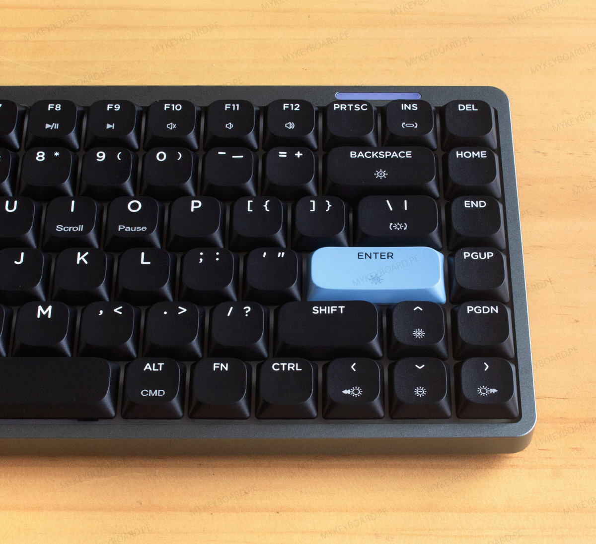 Teclado mecánico Epomaker Luma84 en formato 75% con chasis gris, teclas negras y acentos celestes en fondo de madera.
