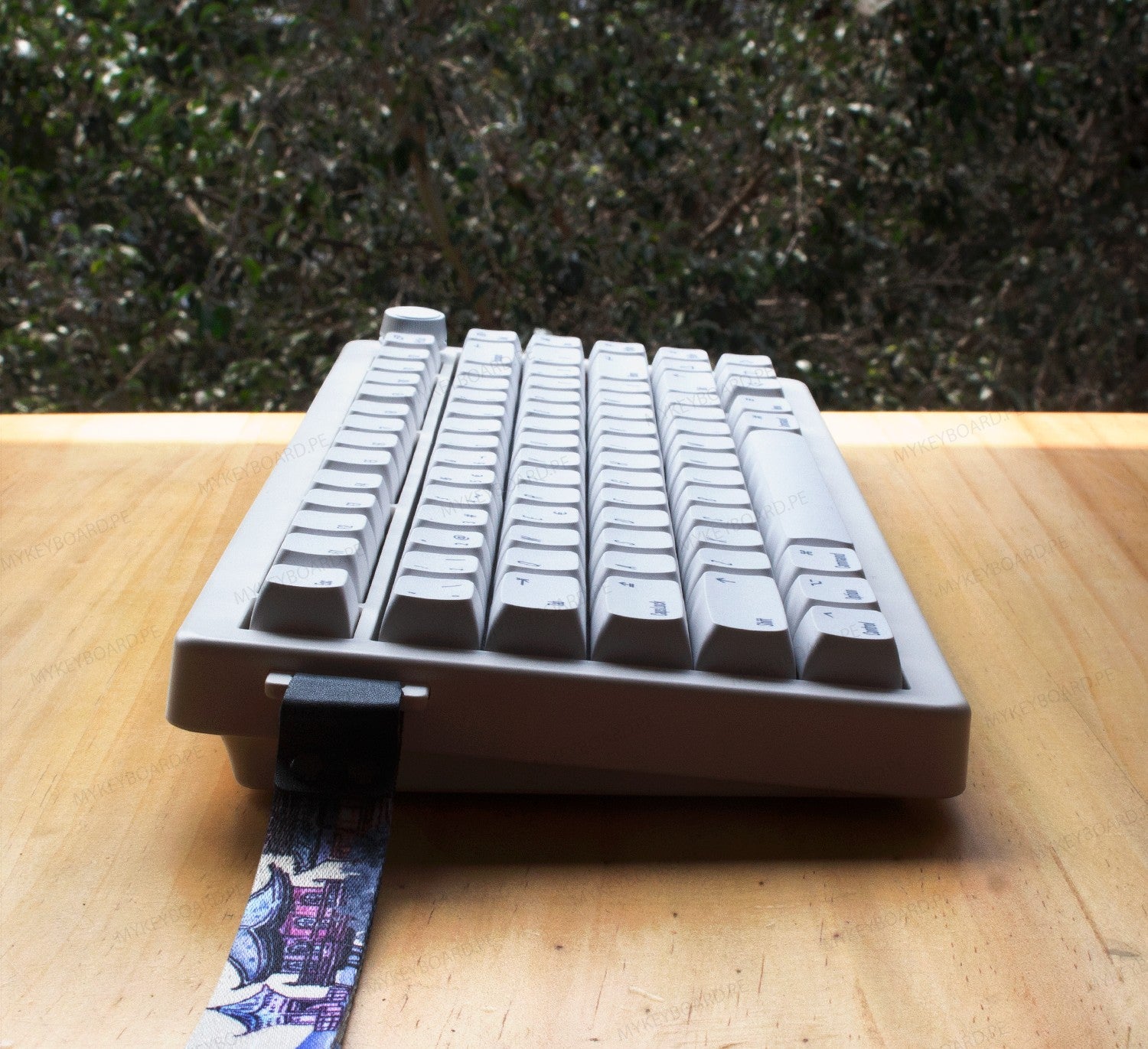 Teclado mecánico MyKeyboard CIDOO QK75 gris de formato 75% con perilla de volumen y correa decorativa sobre mesa de madera