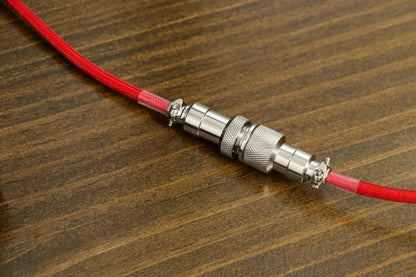 Cable enrollado MyKeyboard EPOMAKER rojo con conector aviador de metal sobre superficie de madera