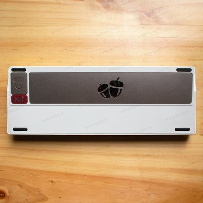 Parte trasera del teclado mecánico MyKeyboard Weikav NUT65 Merlin con acabado blanco y placa decorativa de bellotas.